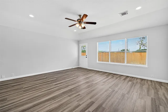 an empty room with wooden floor ceiling fan and windows