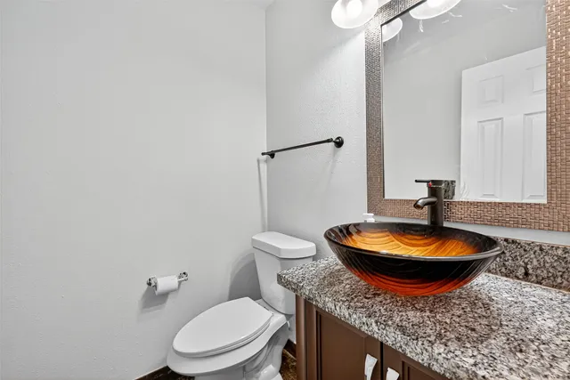 a bathroom with a granite countertop toilet a sink and a mirror