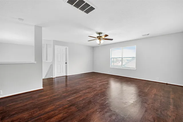 an empty room with wooden floor chandelier fan and windows