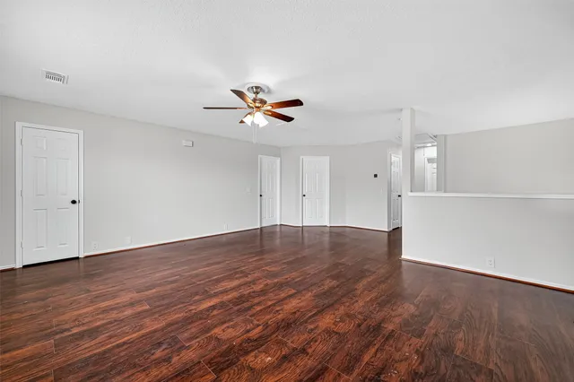a view of an empty room with wooden floor and a ceiling fan