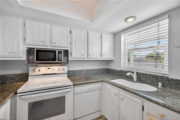 a kitchen with granite countertop white cabinets sink and white stainless steel appliances