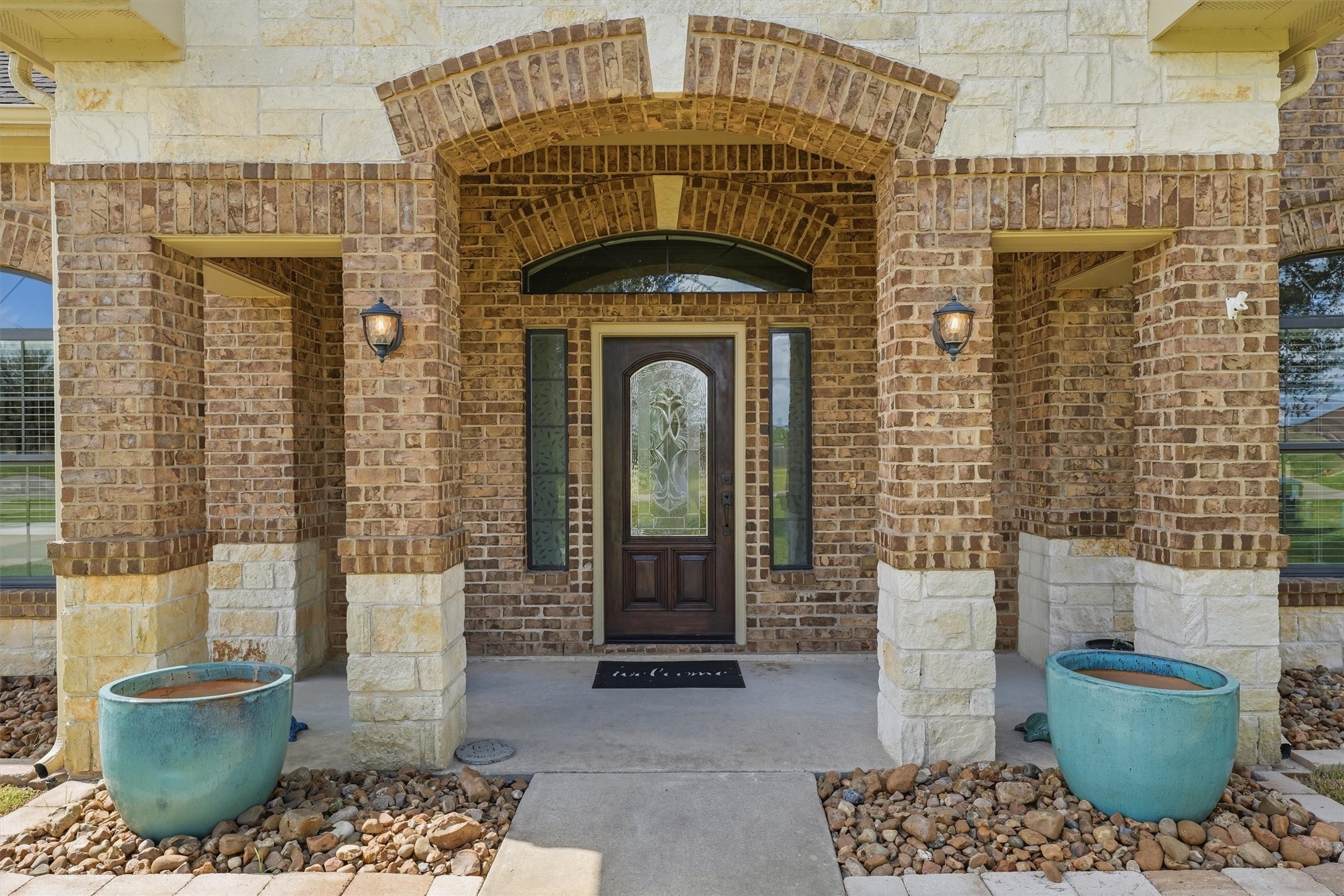 4810 Magnolia Bend Drive Rosharon, TX 77583 - Photo 4 of 40 Classic brick and stone facade with a welcoming arched entryway and wooden door complemented by outdoor lighting fixtures, rocks and vibrant planters.