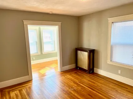 a view of an empty room with window and wooden floor