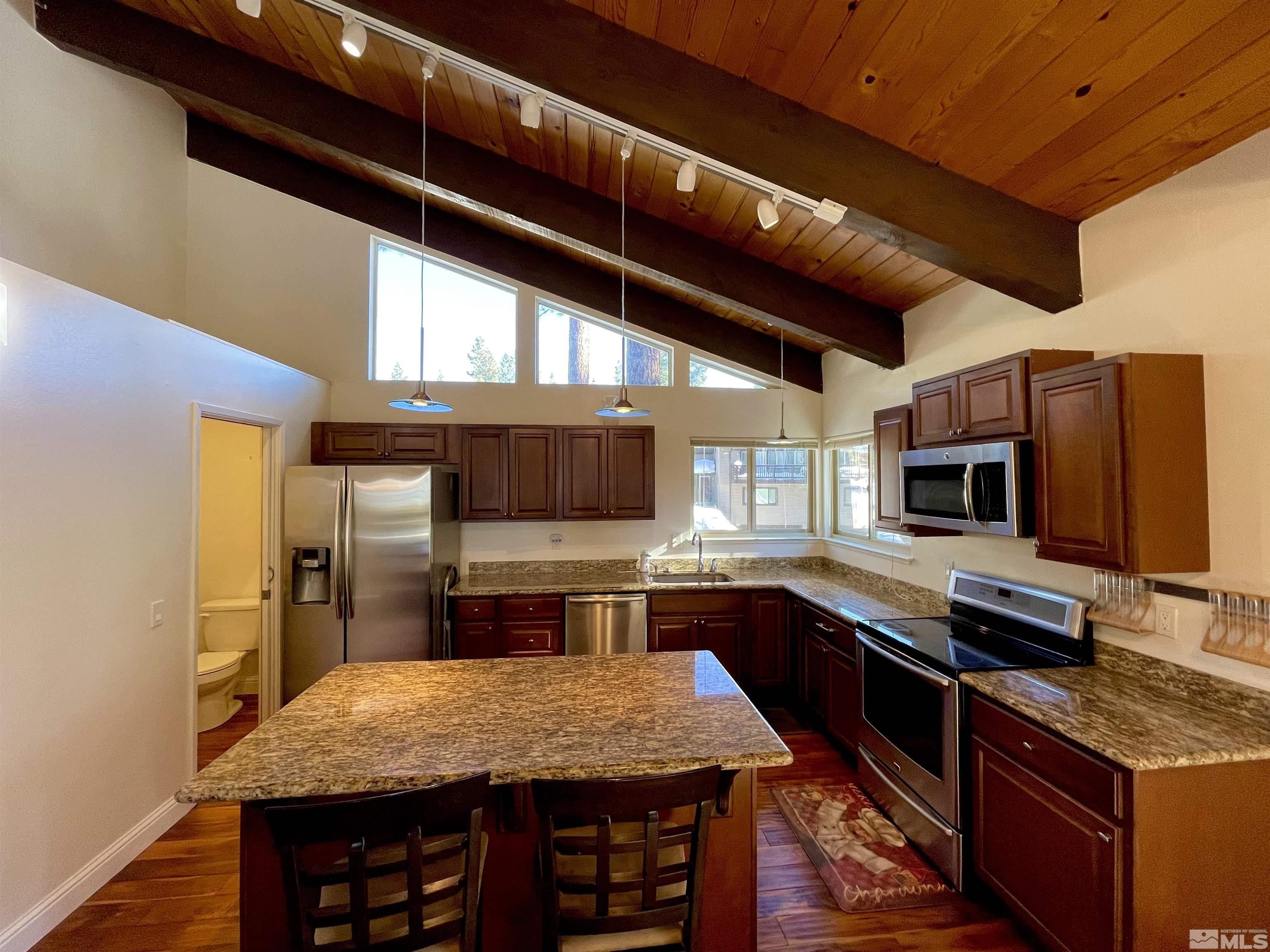 126 Spooner Lane, Unit B Stateline, NV 89449 - Photo 7 of 37 a kitchen with stainless steel appliances kitchen island granite countertop a table chairs in it and wooden floors