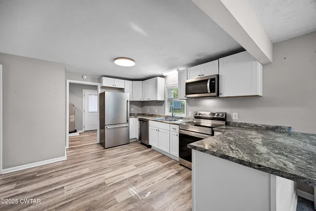 a kitchen with granite countertop a stove top oven a sink dishwasher a refrigerator and white cabinets with wooden floor