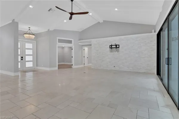 an empty room with chandelier fan and windows