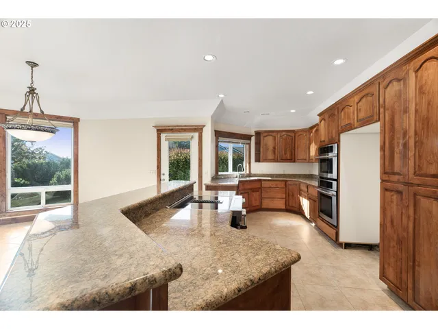 a kitchen with stainless steel appliances granite countertop a refrigerator a stove and a sink with large window