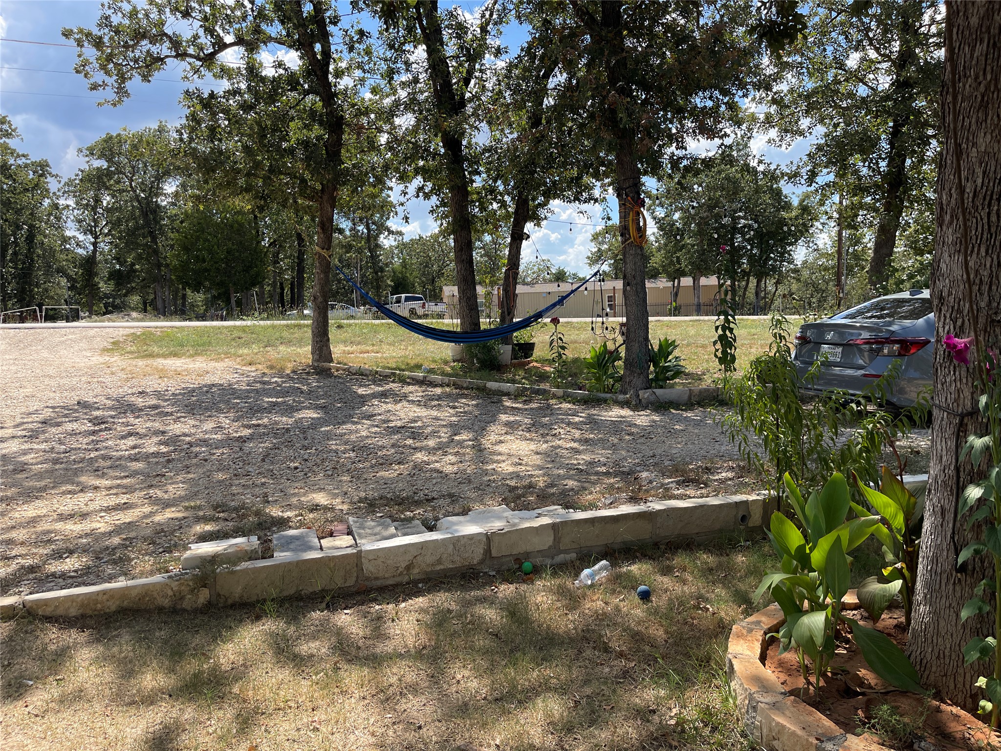 103 Azalea Avenue Elgin, TX 78621 - Photo 16 of 23 Mature trees shade a spacious gravel parking area framed by natural stone retaining borders.