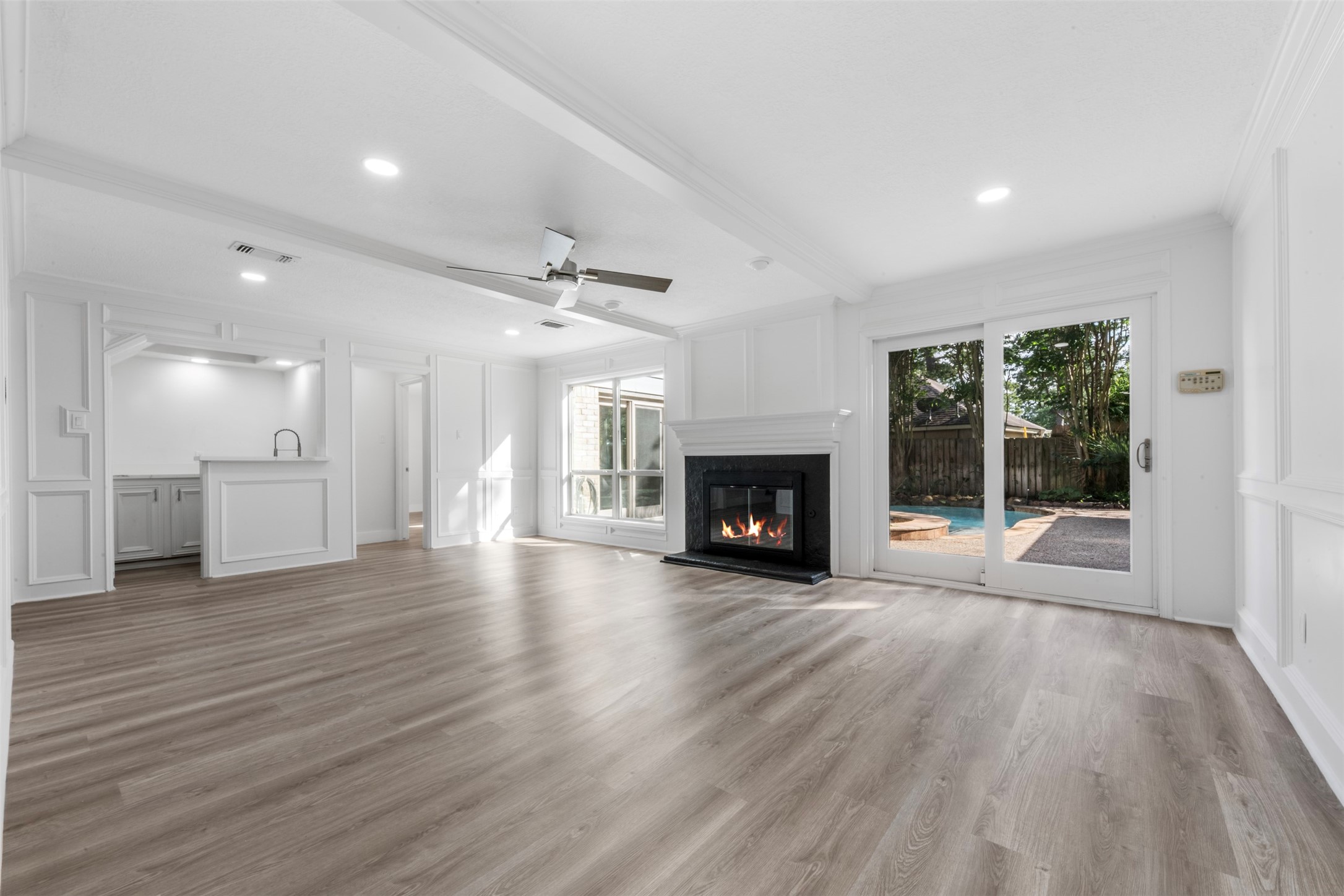 9543 Enstone Circle Spring, TX 77379 - Photo 4 of 50 A spacious living area features modern wood flooring, a cozy fireplace, and large sliding glass doors leading to a backyard with a pool. The open layout flows into a bright kitchen with ample natural light.