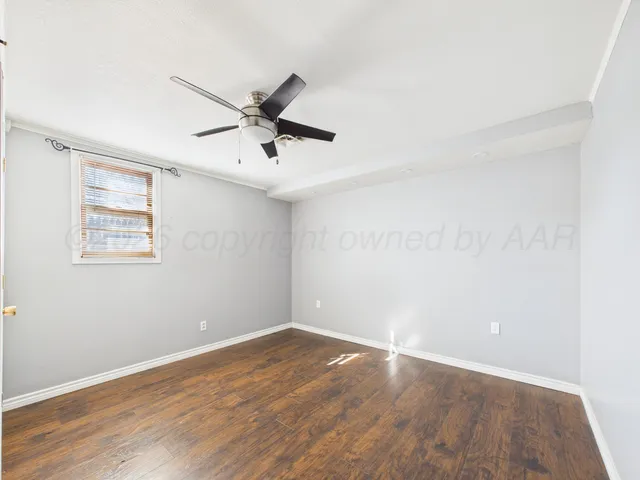 a view of an empty room with wooden floor and a ceiling fan