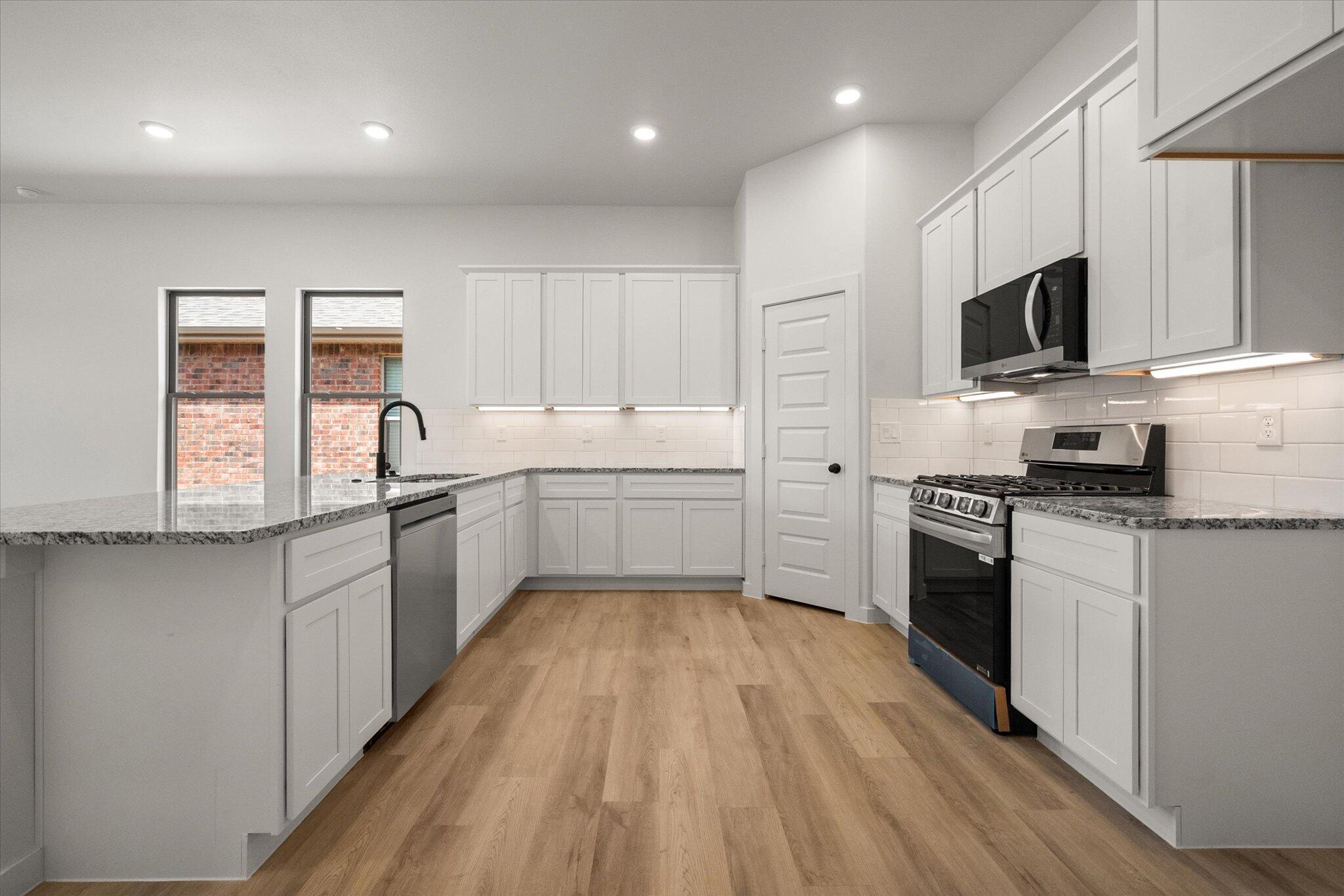 313 East 23rd Street Wolfforth, TX 79382 - Photo 4 of 22 a kitchen with stainless steel appliances a sink dishwasher a stove top oven a refrigerator with grey cabinets and wooden floor