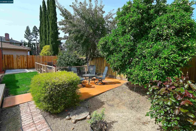 a backyard of a house with table and chairs potted plants and large tree