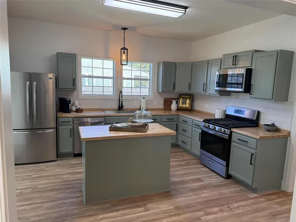a kitchen with kitchen island stainless steel appliances a sink stove refrigerator and a window