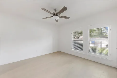an empty room with ceiling fan and windows