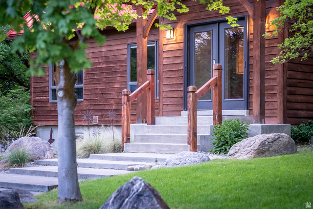 435 Canyon Road Millville, UT 84326 - Photo 2 of 113 Wood-sided exterior featuring concrete steps with wood railings, a dark-framed double-door entry, exterior wall sconce, and mature landscaping