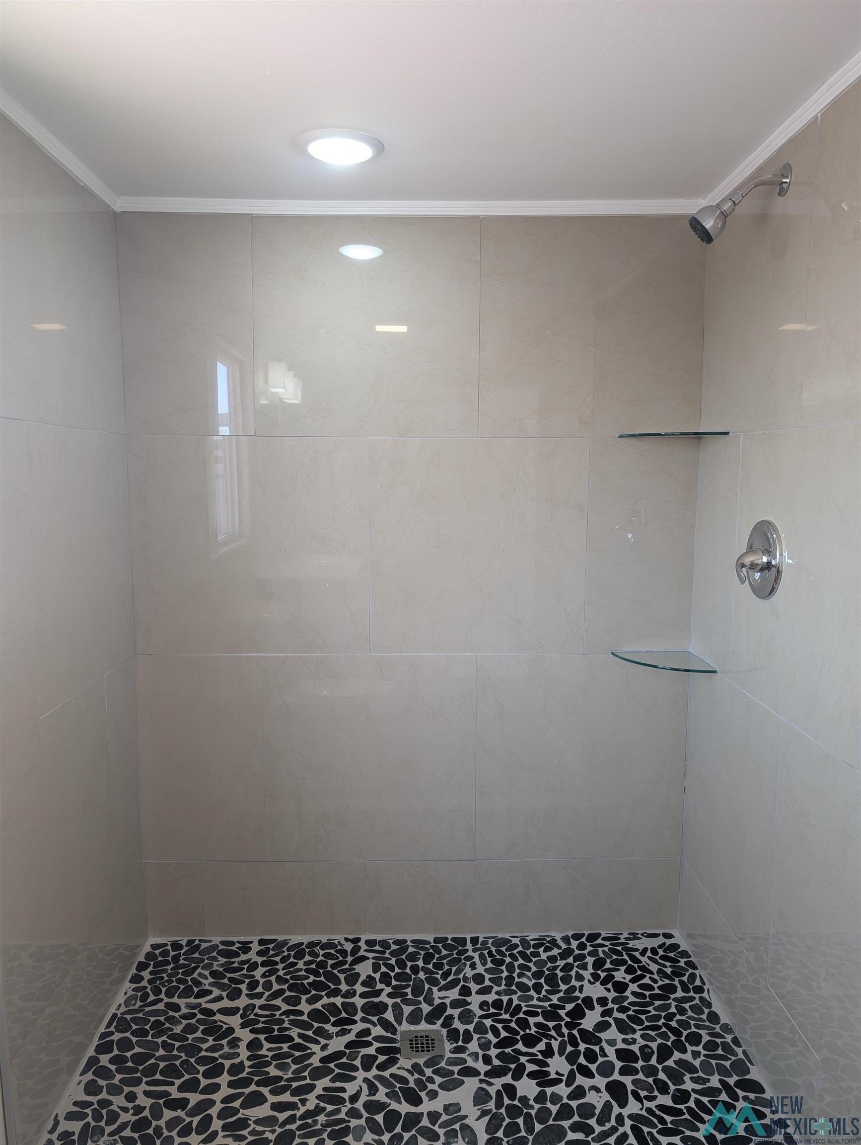 506 Bass Road Elephant Butte, NM 87935 - Photo 6 of 23 Walk-in shower featuring light-toned large format wall tiles, a pebble-stone floor, recessed lighting, and integrated glass shelving