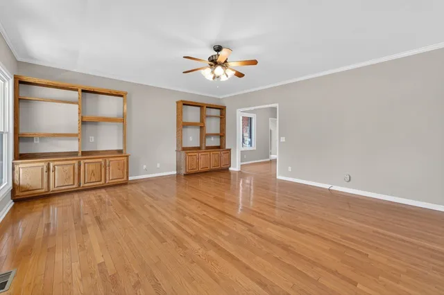 an empty room with wooden floor chandelier fan and windows