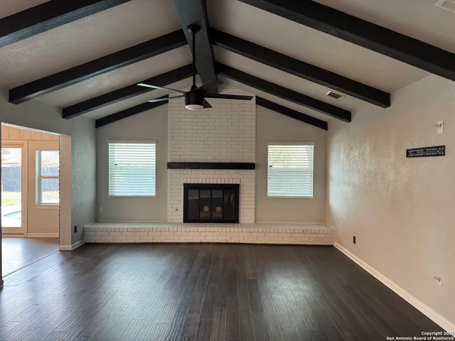 an empty room with wooden floor fireplace and windows