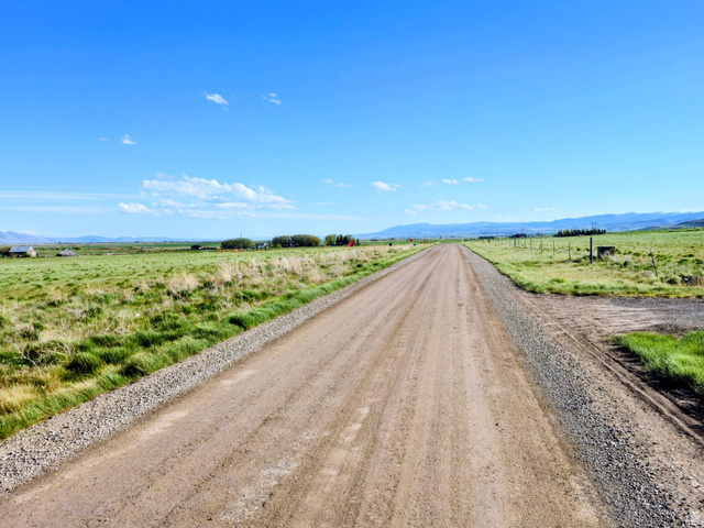 1800 Lower Bern Road, Unit 6 Bern, ID 83220 - Photo 3 of 8 Expansive rural landscape featuring a long unpaved road, surrounding green fields, and distant mountains under a clear blue sky