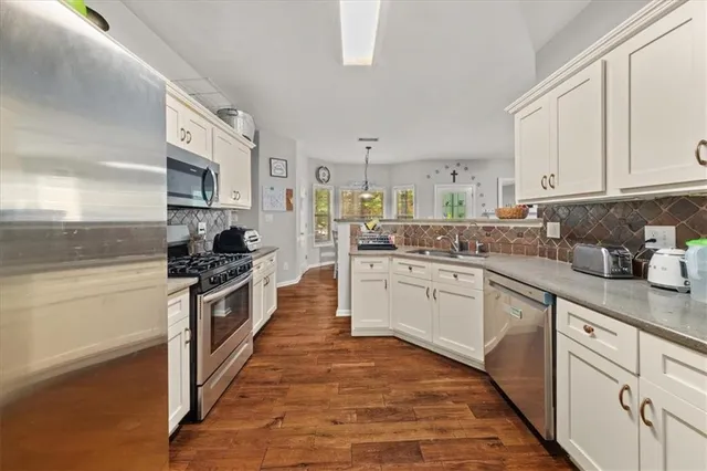 a kitchen with stainless steel appliances granite countertop a stove top oven a sink a refrigerator and white cabinets with wooden floor