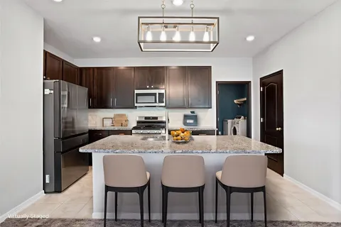 a kitchen with stainless steel appliances granite countertop a dining table chairs refrigerator and cabinets