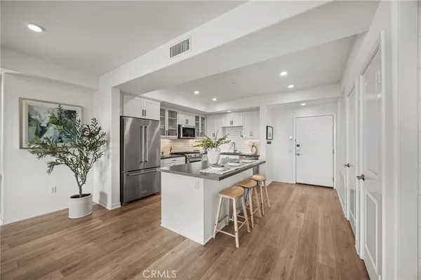 a kitchen with stainless steel appliances kitchen island granite countertop a refrigerator a stove a sink and a dining table with wooden floor