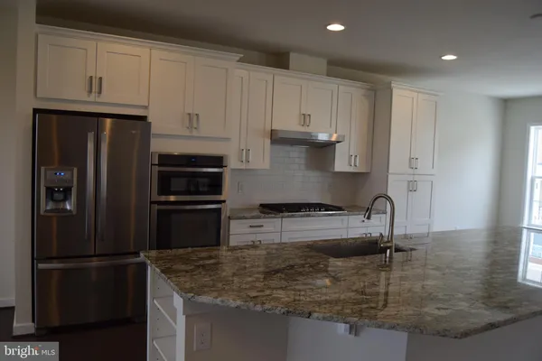 a kitchen with stainless steel appliances granite countertop a refrigerator a stove a sink and white cabinets