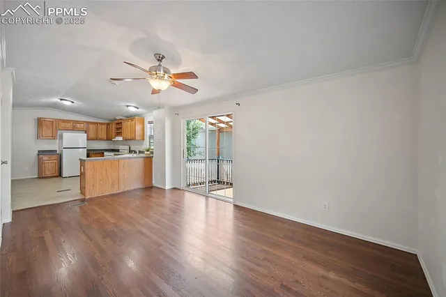 a view of an empty room with wooden floor and a kitchen