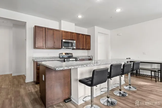 a kitchen with stainless steel appliances granite countertop a stove a sink a microwave a refrigerator and chairs