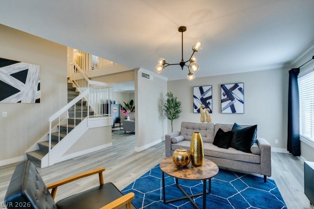 Living room with a chandelier, wood finished floors, and ornamental molding