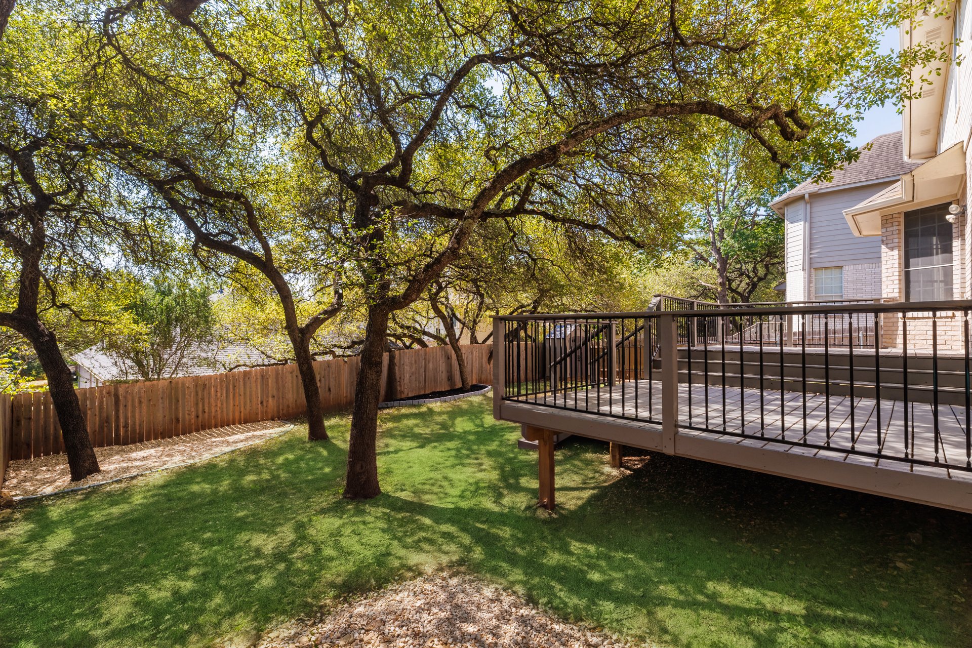 7113 Bending Oak Road Austin, TX 78749 - Photo 34 of 39 Mature shade trees canopy a grassy backyard bordered by wood fencing and a spacious wooden deck.