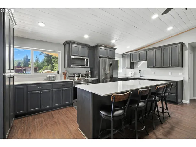 a kitchen with stainless steel appliances granite countertop wooden cabinets a refrigerator a sink a stove a dining table and chairs