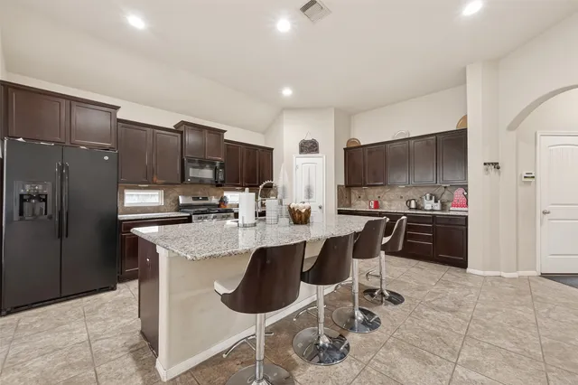 a kitchen with stainless steel appliances a sink a stove a refrigerator cabinets and chairs