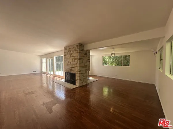 an empty room with wooden floor fireplace and windows