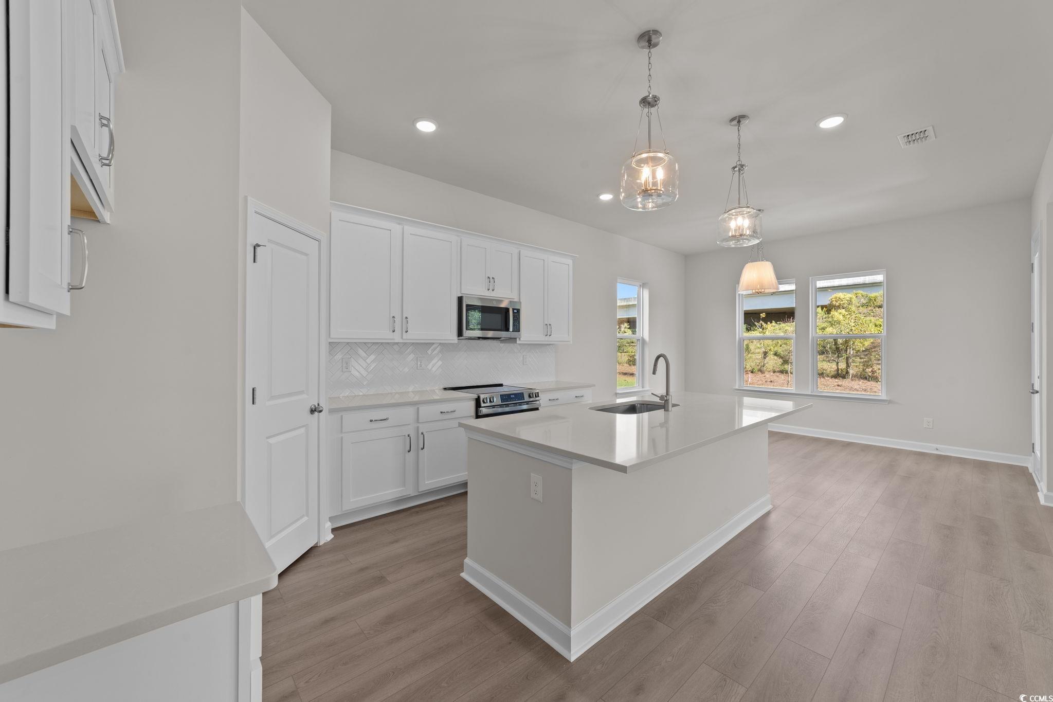 775 Ebb Tide Road Little River, SC 29566 - Photo 12 of 39 Kitchen featuring backsplash, light stone counters, a center island with sink, white cabinetry, and pendant lighting