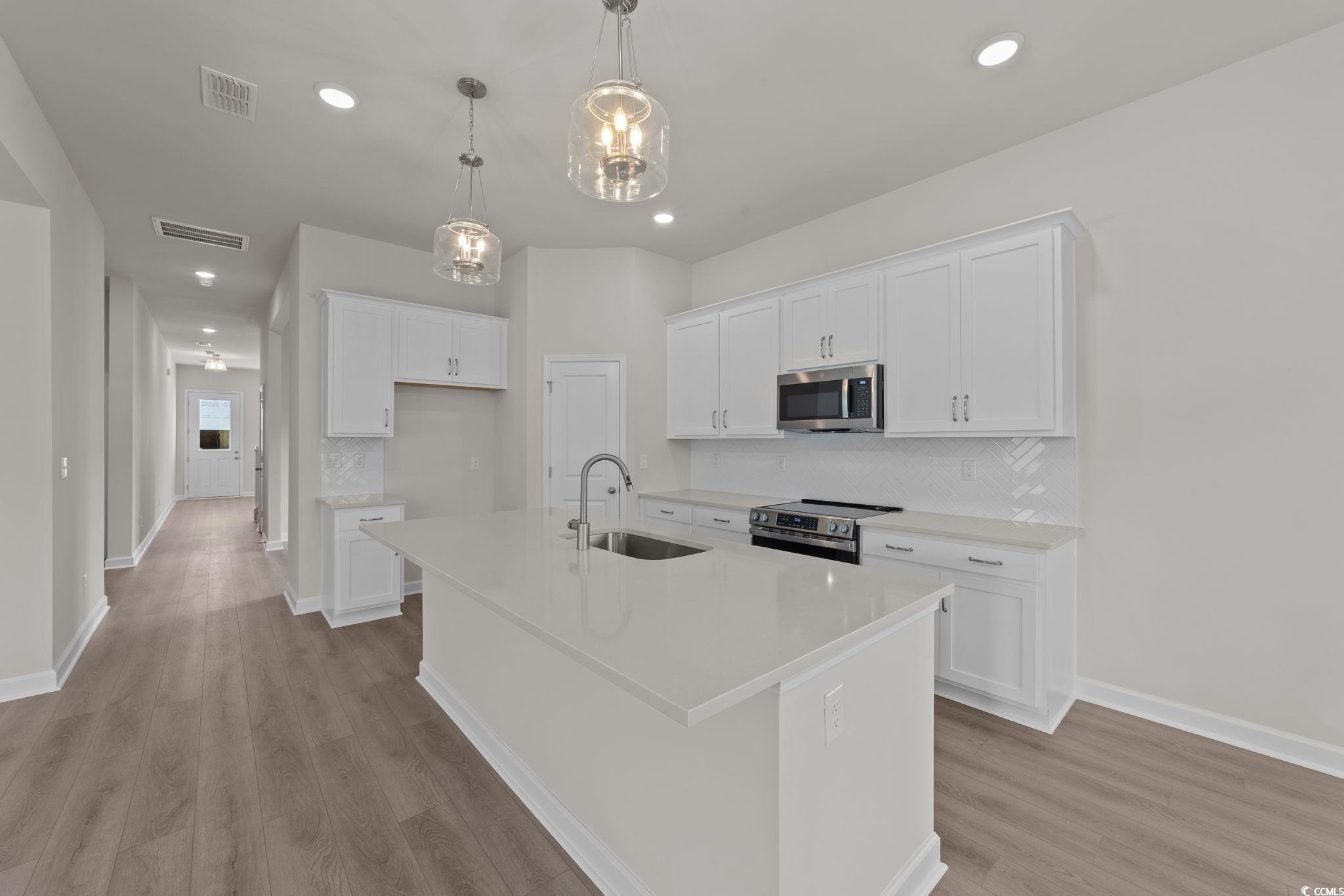 775 Ebb Tide Road Little River, SC 29566 - Photo 13 of 39 Kitchen with white cabinetry, appliances with stainless steel finishes, backsplash, decorative light fixtures, and a center island with sink