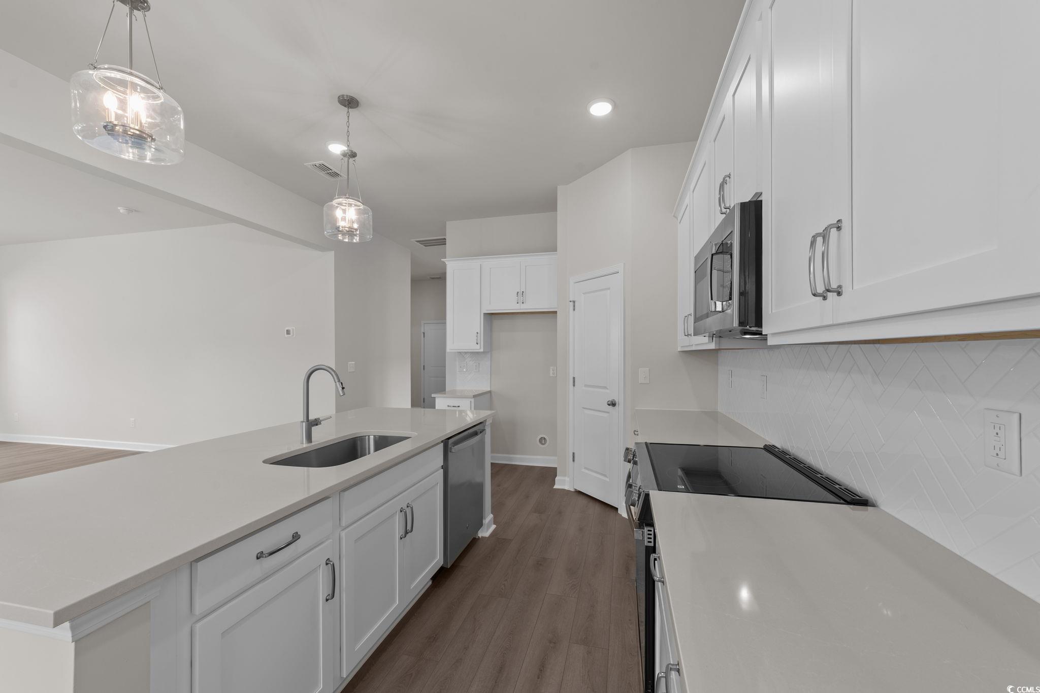 775 Ebb Tide Road Little River, SC 29566 - Photo 14 of 39 Kitchen with a kitchen island with sink, appliances with stainless steel finishes, white cabinets, light stone counters, and hanging light fixtures