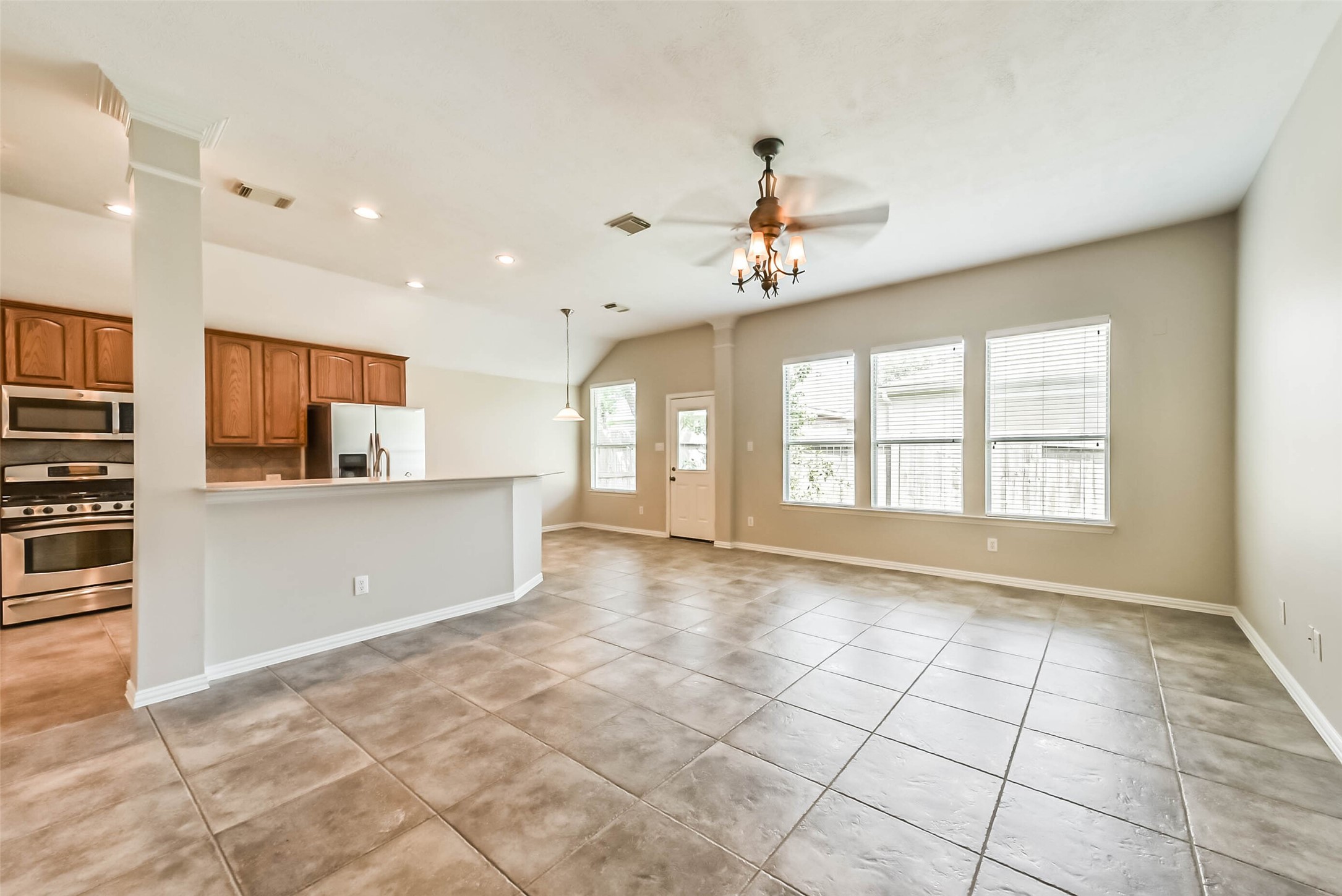 30910 Blue Ridge Park Lane Spring, TX 77386 - Photo 4 of 50 Spacious open-concept living area with large tile flooring and ample natural light, featuring a modern kitchen with stainless steel appliances and warm wood cabinetry.