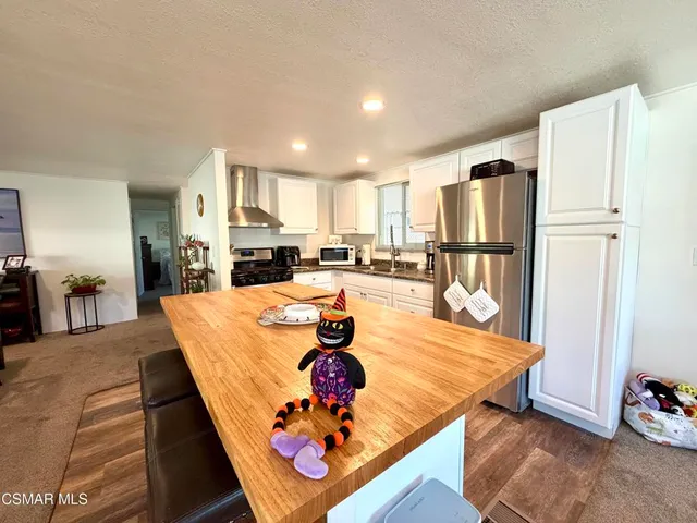 a kitchen with stainless steel appliances kitchen island granite countertop a refrigerator a stove and white cabinets with wooden floor