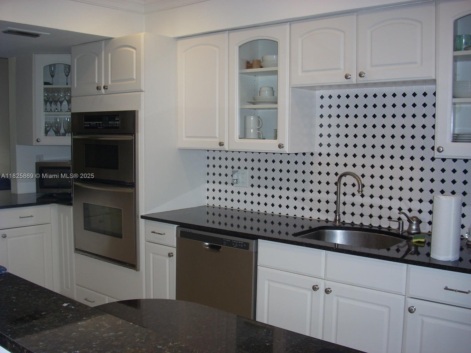 Ojus Miami, FL 33180 - Photo 7 of 15 a kitchen with granite countertop white cabinets and black appliances