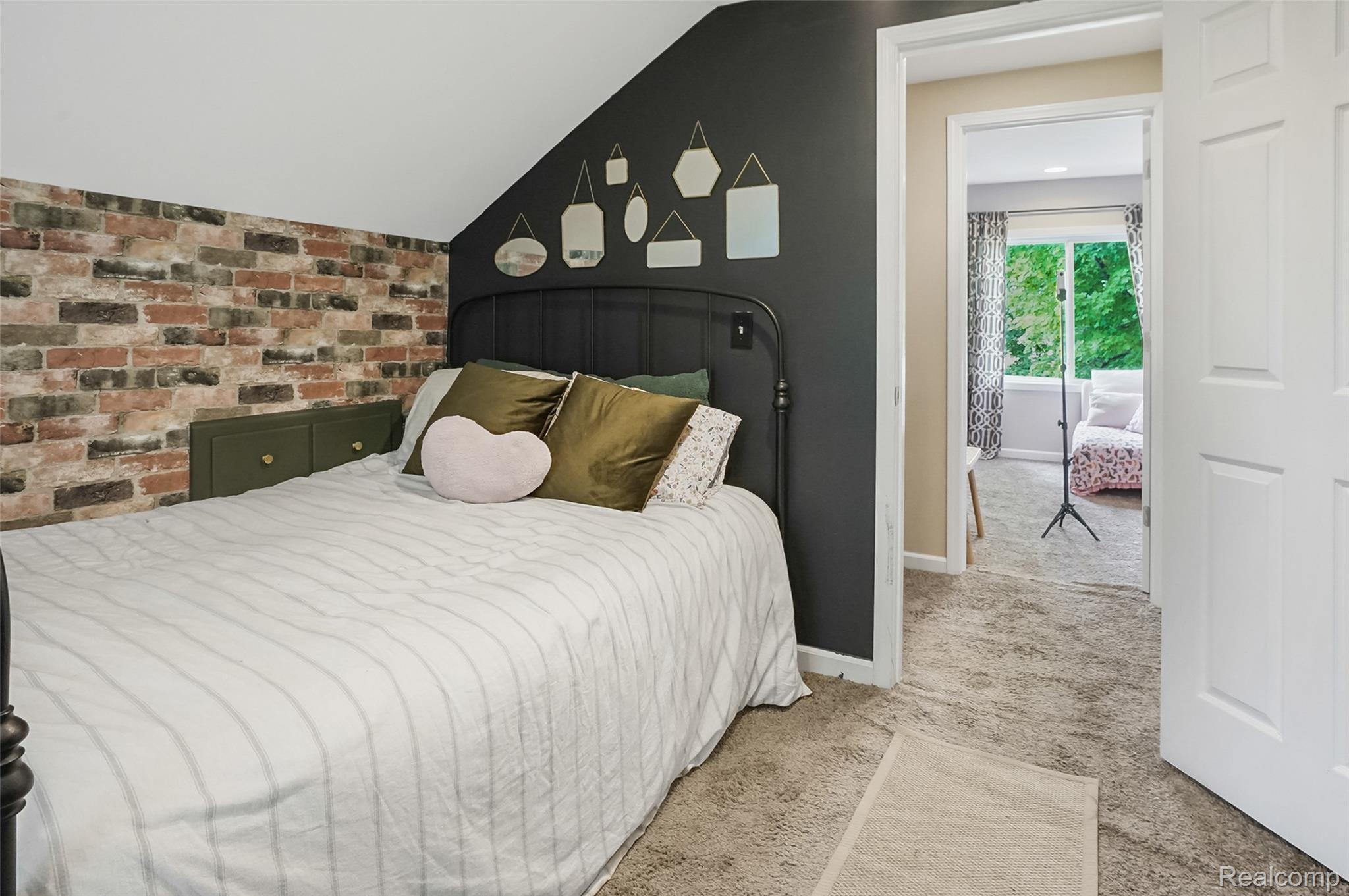 8330 Baldwin Road Gaines, MI 48436 - Photo 17 of 27 Bedroom featuring a pitched ceiling, exposed brick-style wall, built-in cabinetry with brass hardware, and a metal bed frame