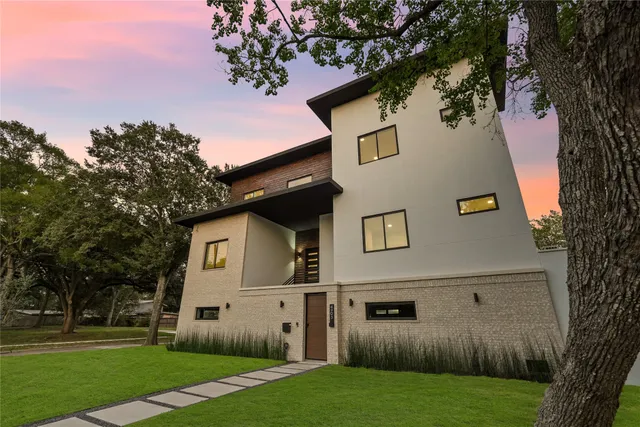 a view of a white house next to a yard with big trees