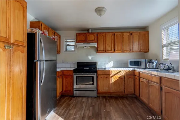 a kitchen with stainless steel appliances granite countertop a refrigerator a sink dishwasher a stove and white countertops with wooden floor