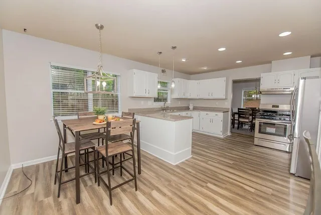 a kitchen with stainless steel appliances granite countertop a stove top oven a sink dishwasher a dining table and chairs with wooden floor