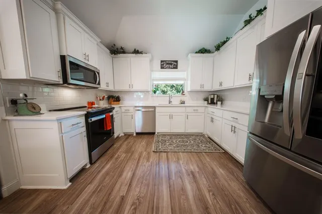 a kitchen with stainless steel appliances granite countertop a refrigerator a sink dishwasher a stove top oven a refrigerator with white cabinets and wooden floor