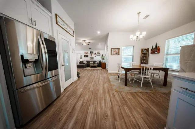 a kitchen with stainless steel appliances a refrigerator a stove top oven a dining table and chairs with wooden floor