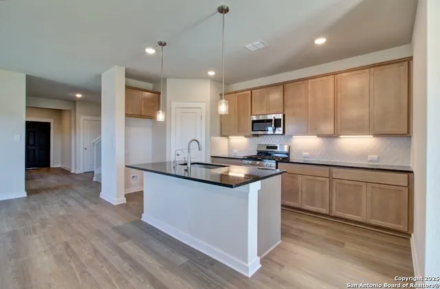 a kitchen with stainless steel appliances granite countertop wooden cabinets a sink a stove a refrigerator and island