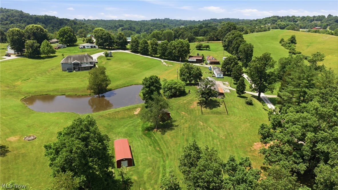 89 Dagg Road Parkersburg, WV 26101 - Photo 39 of 45 Expansive green acreage featuring a large pond, mature trees, a red barn, and a multi-level residence with a rear deck