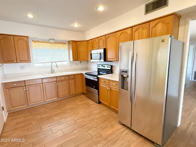 a kitchen with stainless steel appliances granite countertop a refrigerator a sink dishwasher and white cabinets with wooden floor
