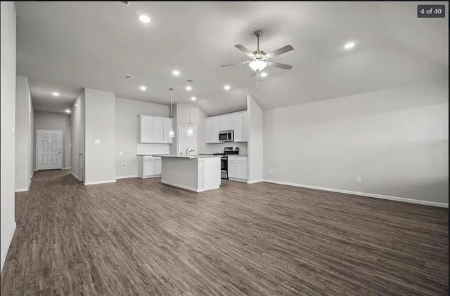 a view of an empty room with wooden floor and kitchen view